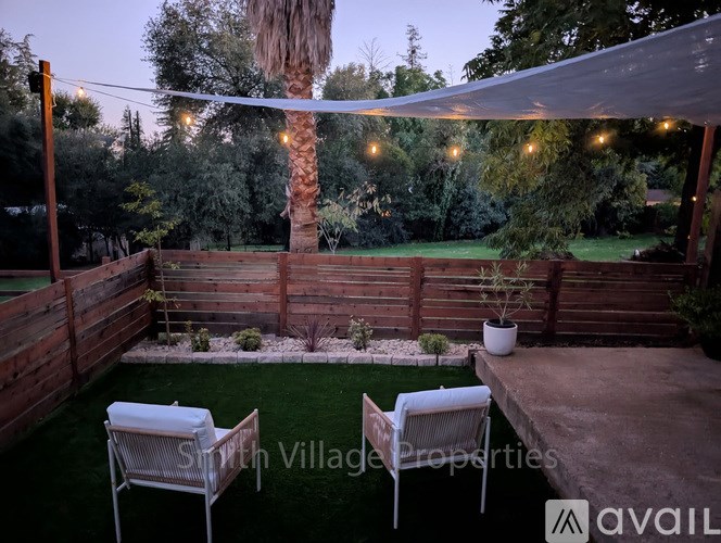 A backyard with a patio, a table, two chairs and a tree.