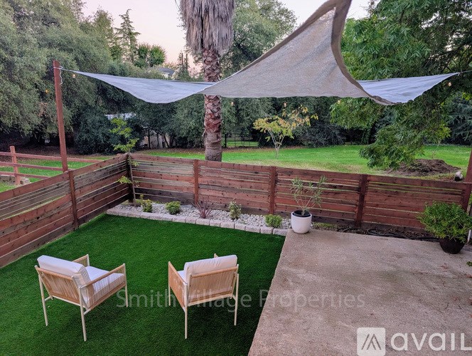 A backyard with a wooden fence, two chairs, and a white umbrella.