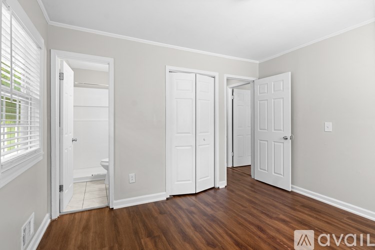 A room with white walls and wooden floors, with three doors and one window with blinds.