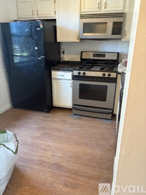 A kitchen with a black fridge, white oven, and white cabinets.