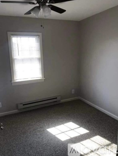 A room with a ceiling fan, window with blinds, and a radiator on the wall.