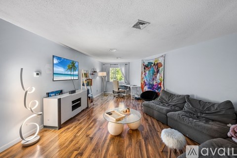 A living room with a grey couch, a wooden floor, and a painting of a beach scene on the wall.