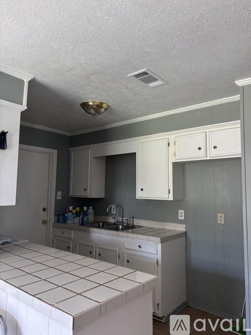 A bathroom with a white tiled counter top and white cabinets.