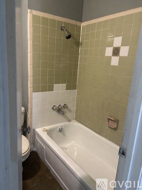 A white bathtub is in a bathroom with green tiles.