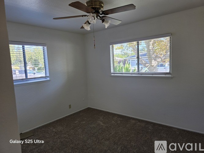 A room with a ceiling fan and two windows.