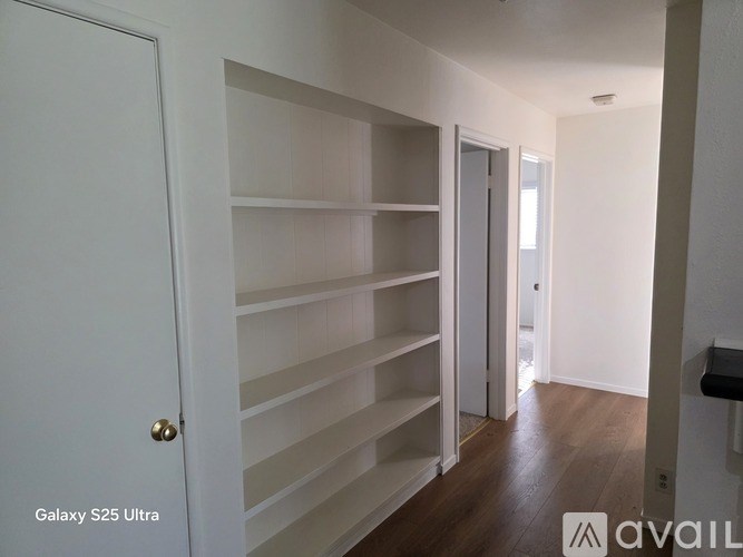 A white door with a gold handle is on the left side of a hallway with shelves on the right.