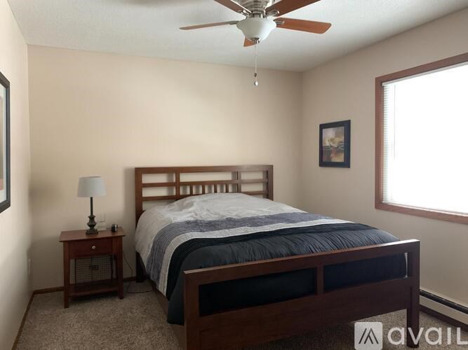 A bedroom with a bed, a ceiling fan, and a nightstand with a lamp.