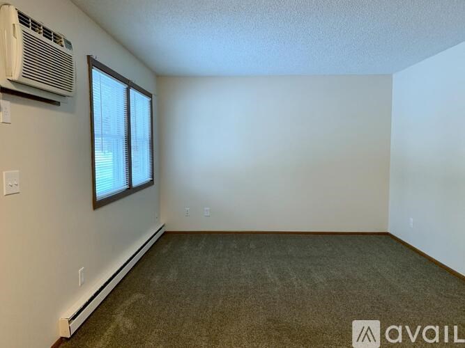 A room with a carpeted floor, a window with blinds, and a wall-mounted air conditioner unit.