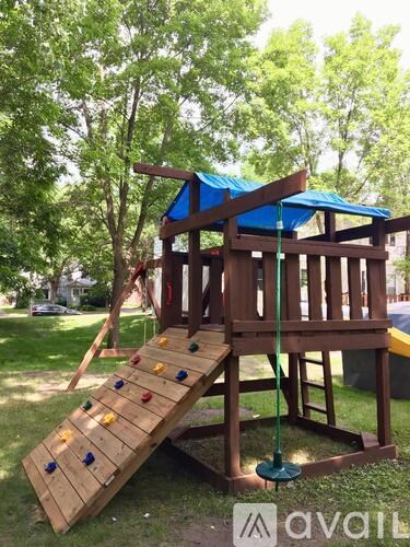 A wooden swing set with a blue canopy is in a grassy area.