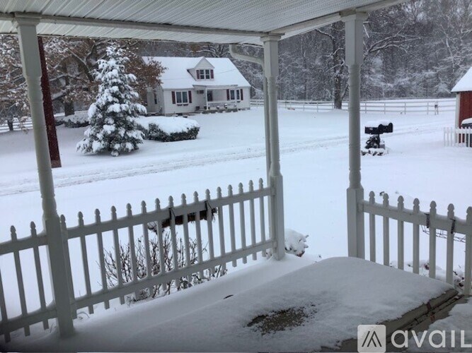 A snow-covered porch with a white picket fence and a house in the background.