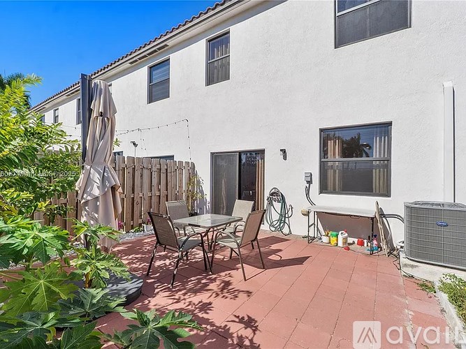 A patio with a table and chairs is surrounded by a wooden fence and green plants.