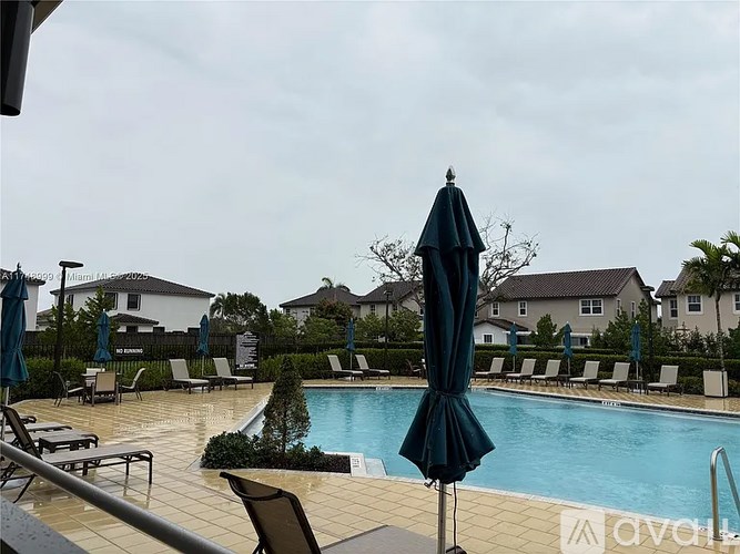 A pool with a black umbrella in the foreground and a house in the background.