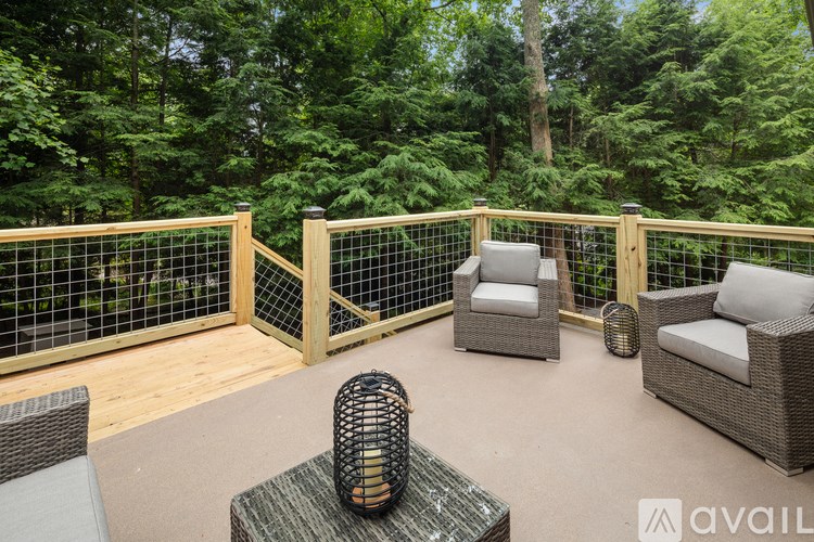 A patio with wicker furniture and a railing overlooking a forest.