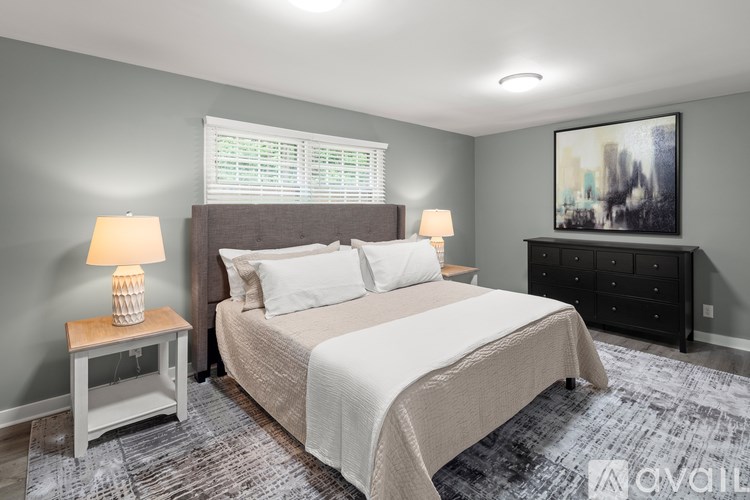 A bedroom with a large bed, a nightstand with a lamp, and a painting on the wall.