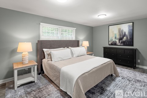 A bedroom with a large bed, a nightstand with a lamp, and a painting on the wall.