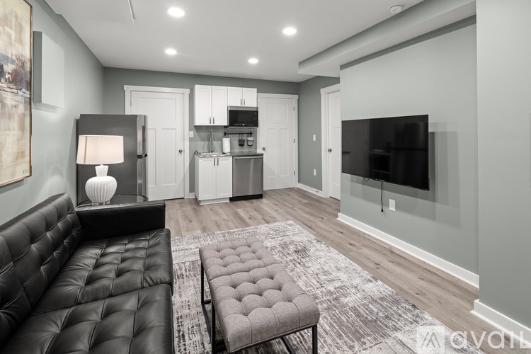 A black leather sofa sits in a well-lit living room with a television and a kitchen area in the background.