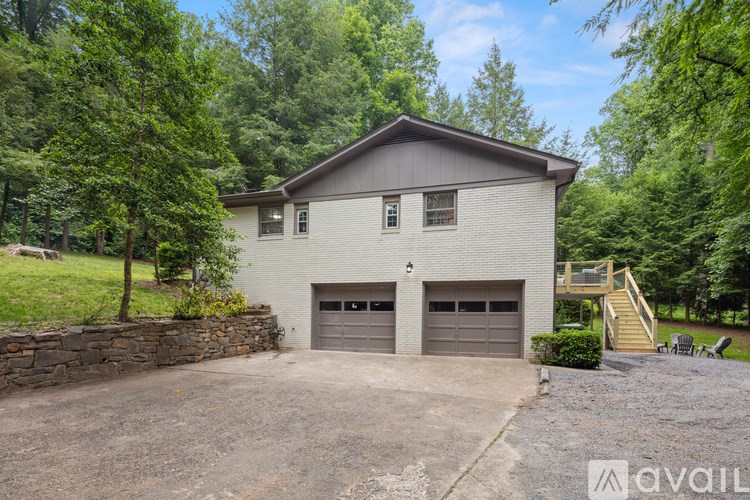 A house with a stone wall and two garages is surrounded by trees.
