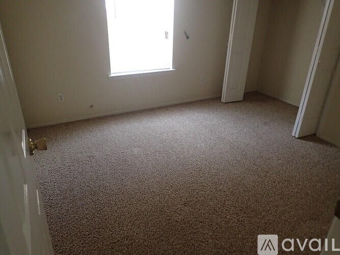 A carpeted room with a window and a door.