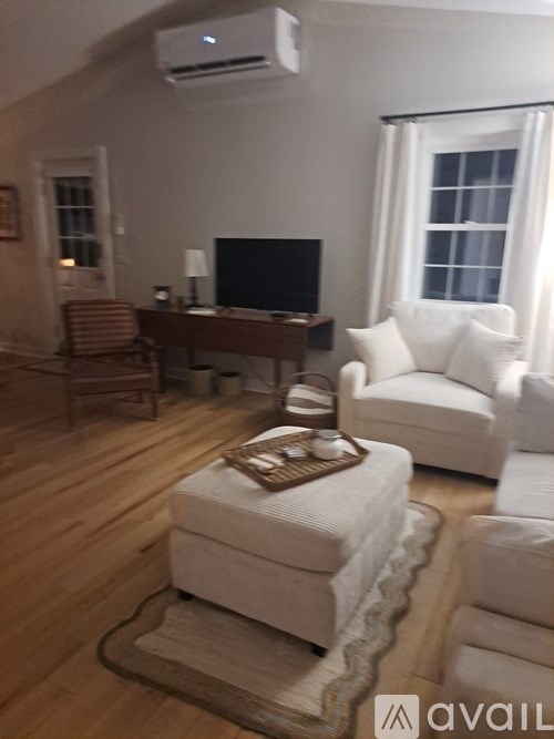 A living room with a white chair, a brown ottoman, and a wooden table.