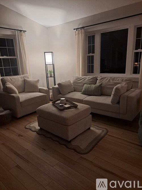 A living room with a white couch, a chair, a small ottoman, and a floor lamp.