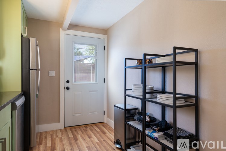 A kitchen with a refrigerator, a door, and a shelf with plates on it.