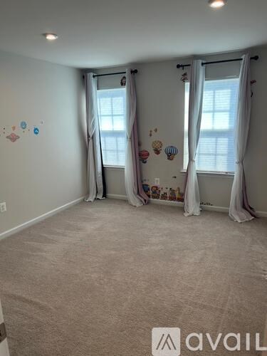 A room with carpeted floor and two windows with curtains.
