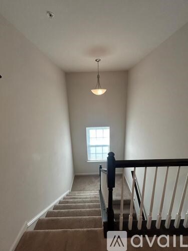 A staircase with a carpeted runner and a black railing leads to a window.