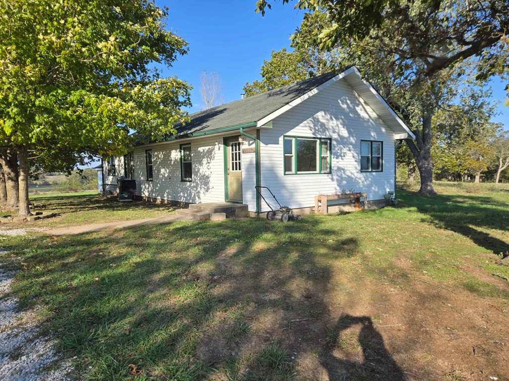 A white house with a green roof is surrounded by trees and grass.