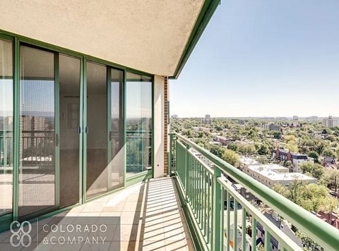 A balcony with green railings overlooks a cityscape.