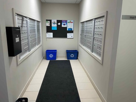 A hallway with mailboxes on the wall and two blue bins on the floor.
