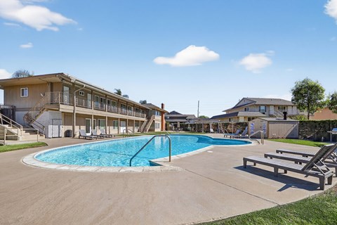 A large outdoor swimming pool surrounded by a grassy area and a building in the background.