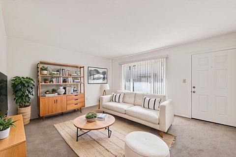 A living room with a white couch, a wooden coffee table, and a large window with blinds.