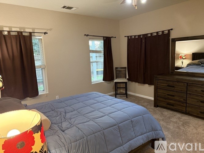 A bedroom with a blue bedspread and brown curtains.