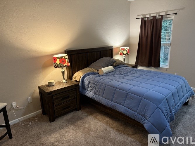 A bedroom with a blue bedspread and two lamps on nightstands.
