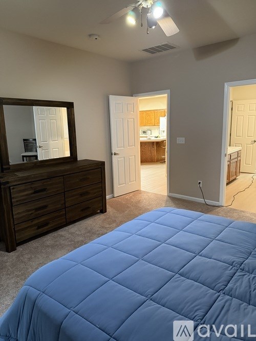 A bedroom with a blue bedspread and a wooden dresser with a mirror.