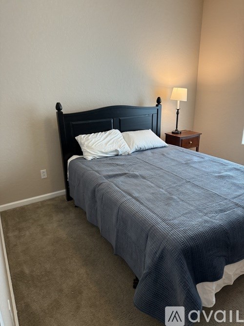 A bed with a dark headboard and a grey bedspread with two white pillows.