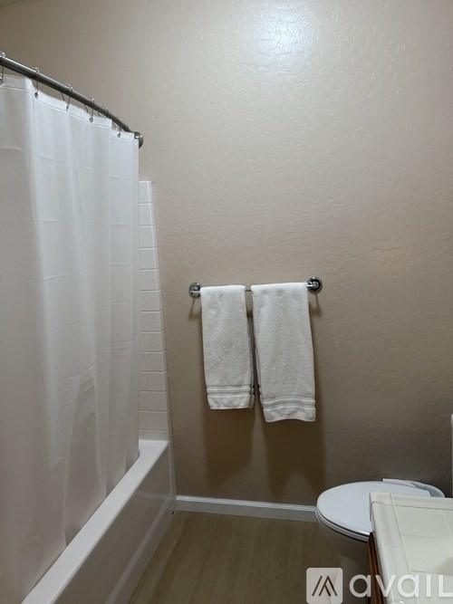 A bathroom with a toilet, a towel rack with two white towels, and a shower with a white curtain.
