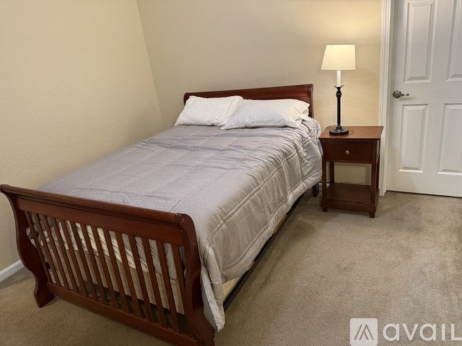 A bed with a grey comforter and a wooden headboard is in a room with a carpeted floor.