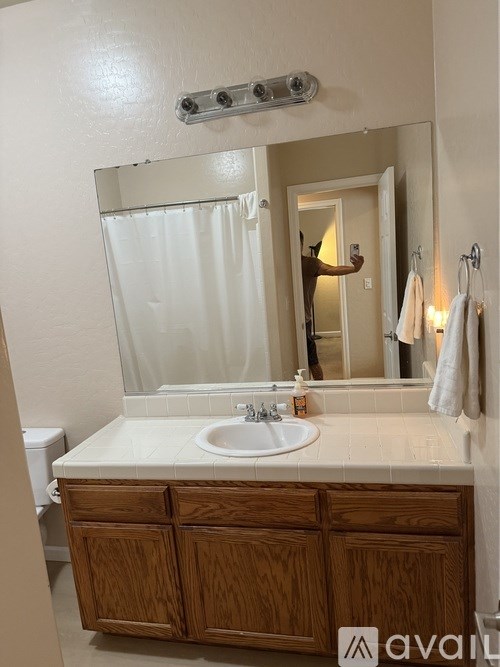 A person is taking a selfie in a bathroom with a white sink and wooden cabinet.