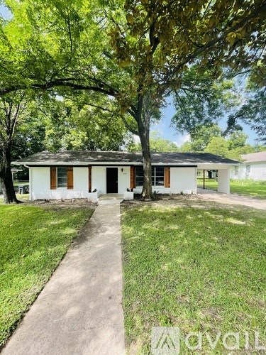A white house with a brown roof and a tree in front of it.