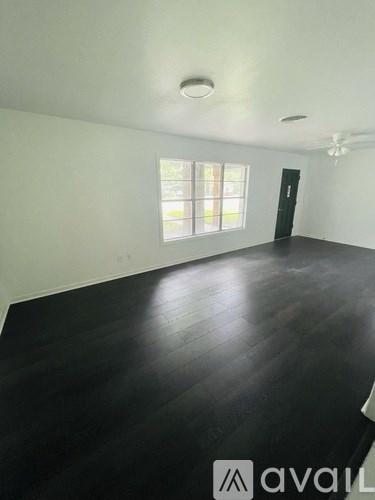 A room with black flooring and a window with a view of a tree.