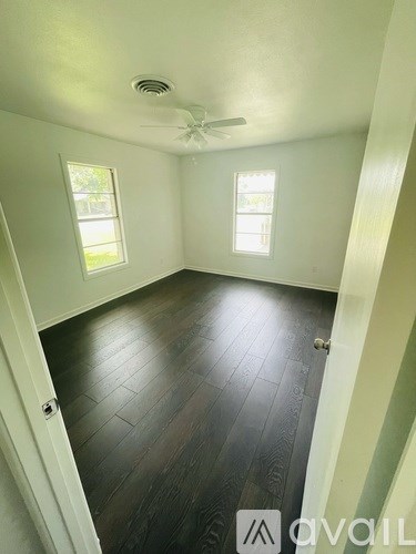 A room with a ceiling fan and two windows.