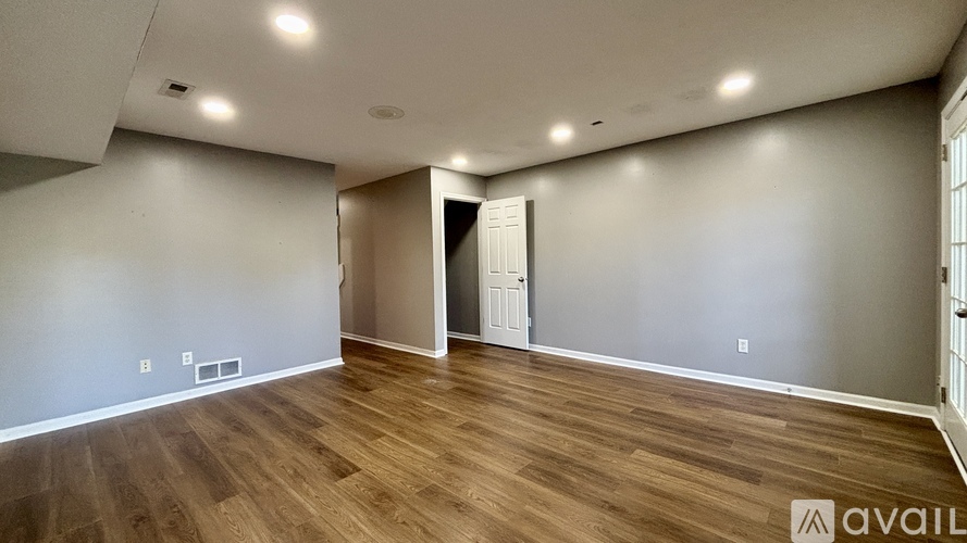 A spacious room with wooden flooring and a doorway leading to another room.