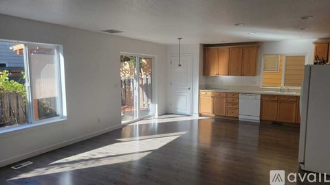 A spacious living room with wooden floors and a kitchen area in the background.