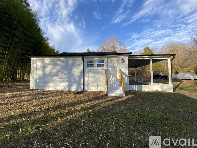 A white building with a black roof is surrounded by trees and grass.