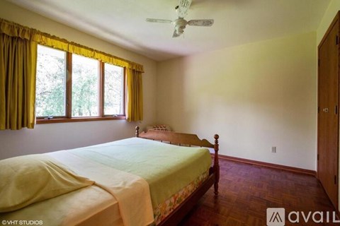 A bedroom with a bed, a ceiling fan, and a window with yellow curtains.