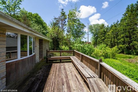 A wooden deck leads to a house with a view of a green forest.