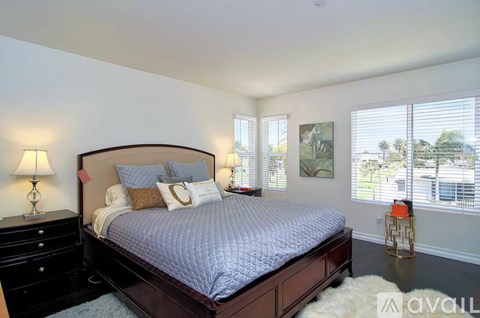 A bedroom with a large bed, a nightstand with a lamp, and a window with blinds.