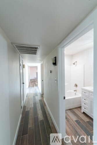 A long hallway with a white door on the right and a white bathroom with a tub and sink.