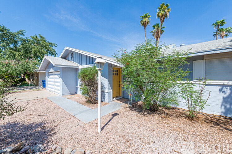 A house with a yellow door is surrounded by a gravel driveway and palm trees.